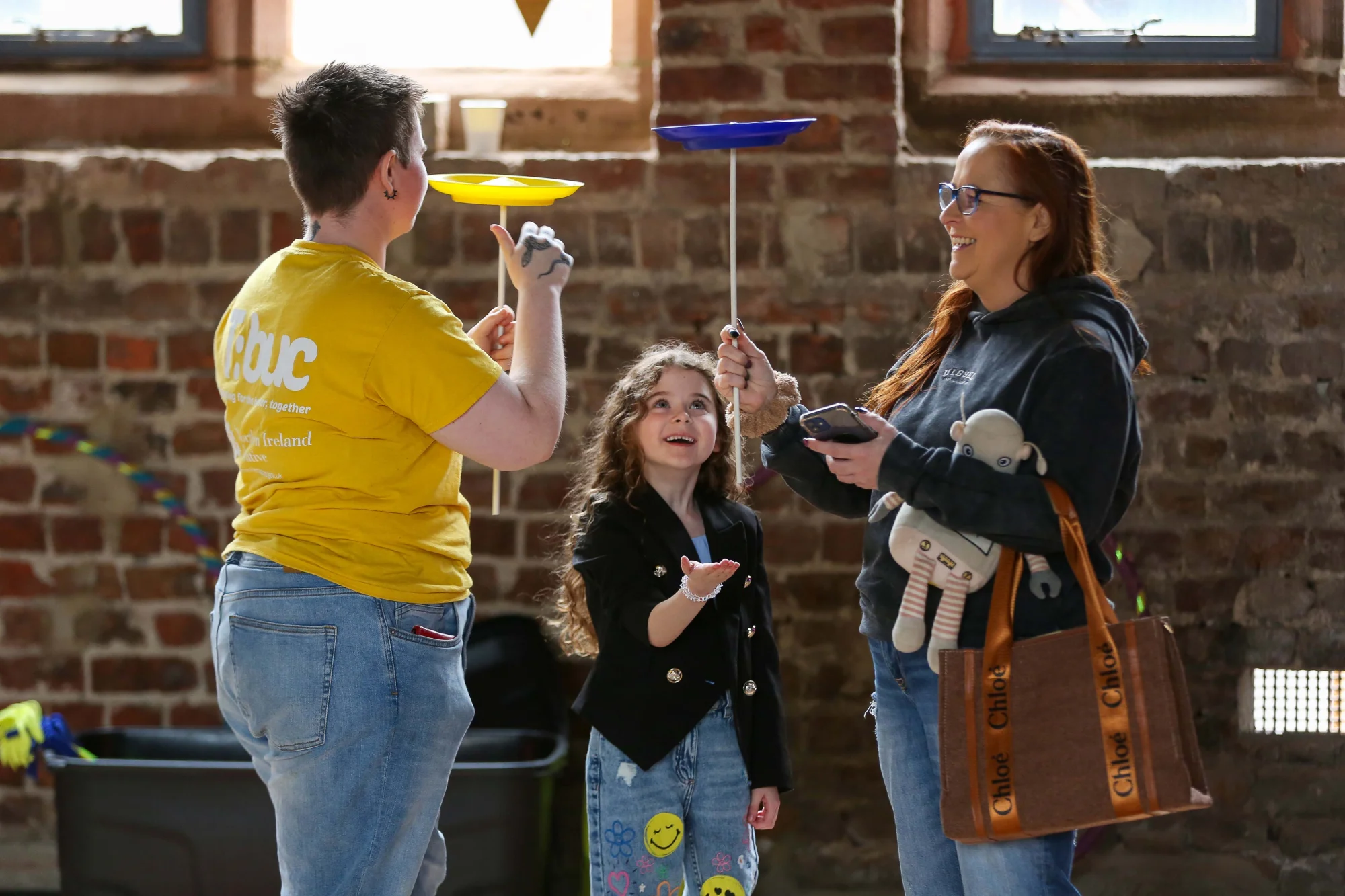 A group of three people learn to spin plates on sticks at the Cathedral School